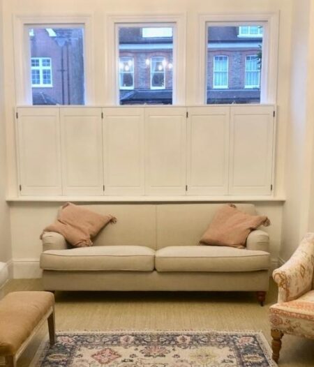 cafe style solid shutters in a sitting room with beige sofa and brown cushions