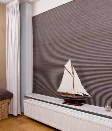 corded honeycomb blind in dark colour with a model boat on the window sill