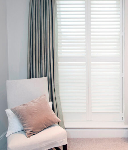 window with white full height mdf shutters and little chair with cushions