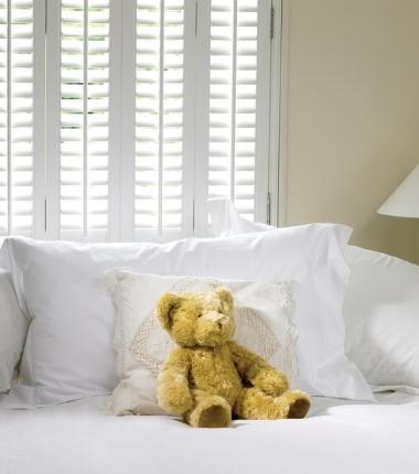 teddy bear on a white sofa representing cleanliness of the white shutters in the back